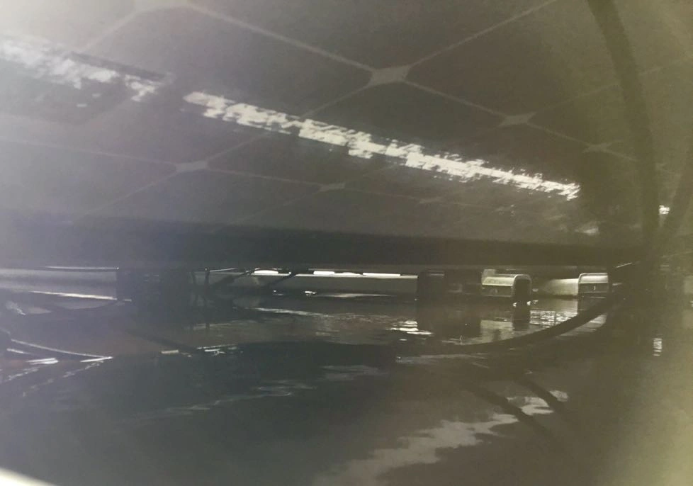 Onderaanzicht van zonnepaneel op plat dak met een laag water waarin kabels en connectoren hangen: zo moet het dus niet!